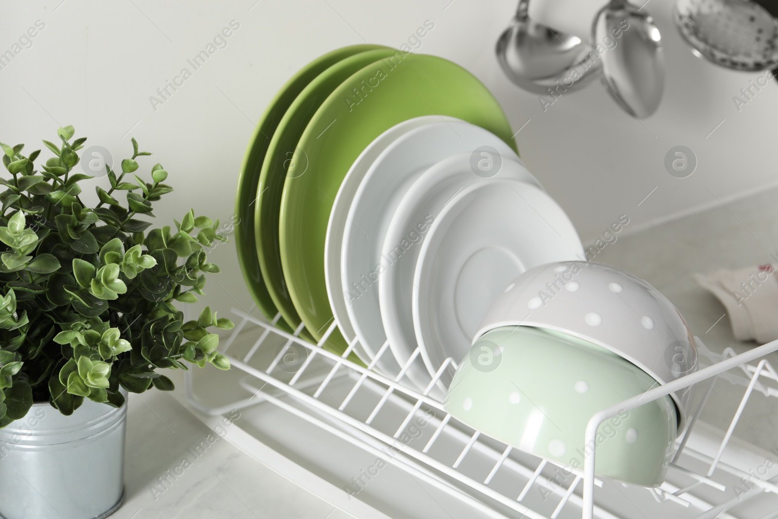 Photo of Drainer with different clean dishware and houseplant on light table in kitchen