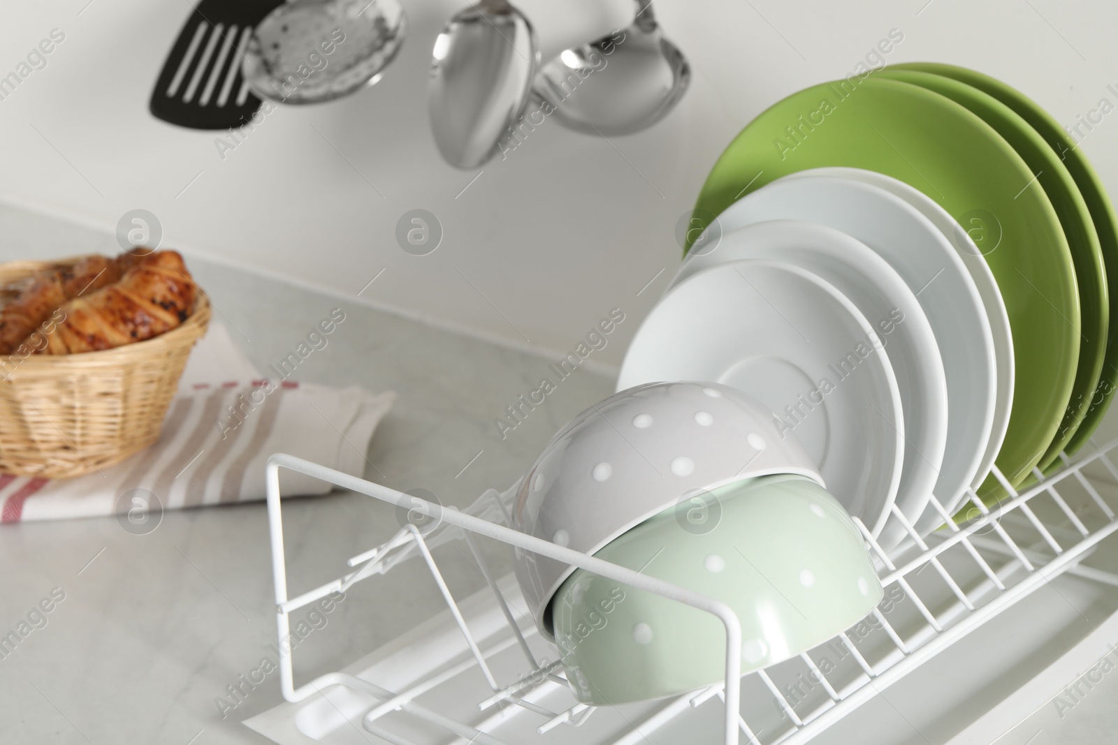 Photo of Drainer with different clean dishware on light table in kitchen