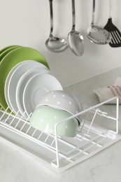 Photo of Drainer with different clean dishware on light table in kitchen