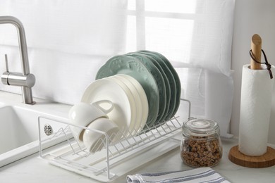 Photo of Drainer with different clean dishware and cups on white table in kitchen