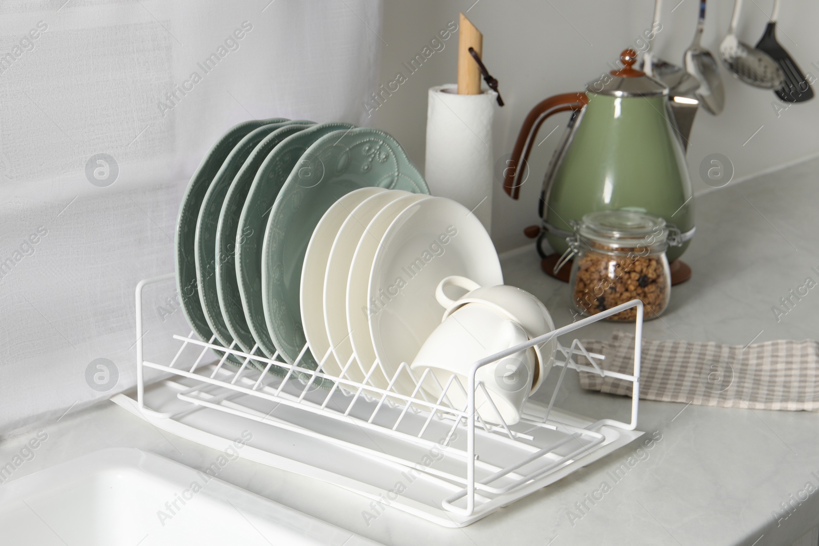 Photo of Drainer with different clean dishware and cups on white table in kitchen