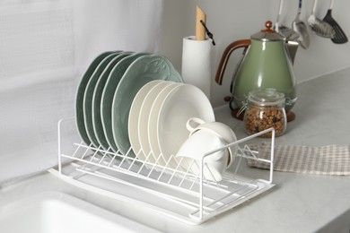 Photo of Drainer with different clean dishware and cups on white table in kitchen