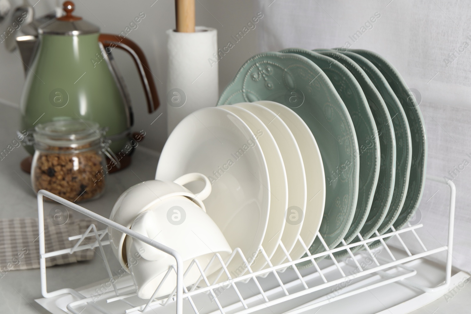 Photo of Drainer with different clean dishware and cups on white table in kitchen