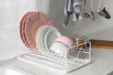 Drainer with different clean dishware on white table in kitchen