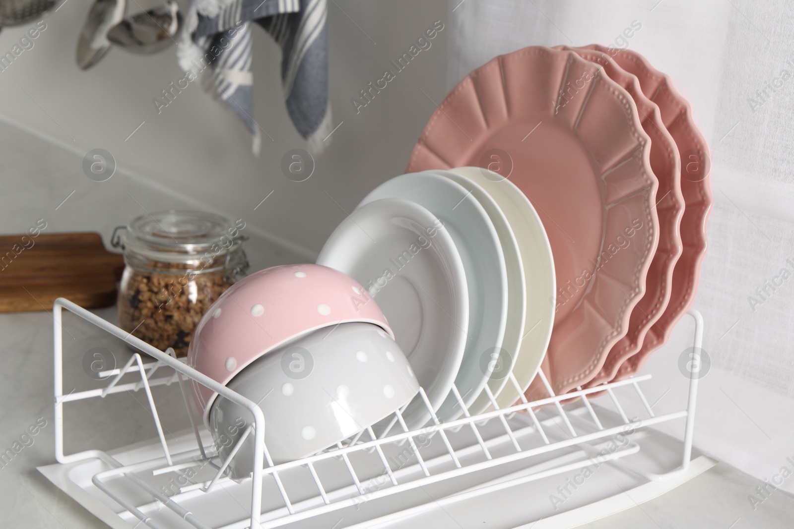 Photo of Drainer with different clean dishware on white table in kitchen