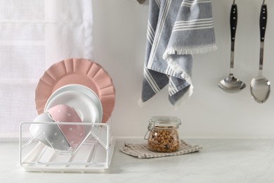 Drainer with different clean dishware on white table in kitchen