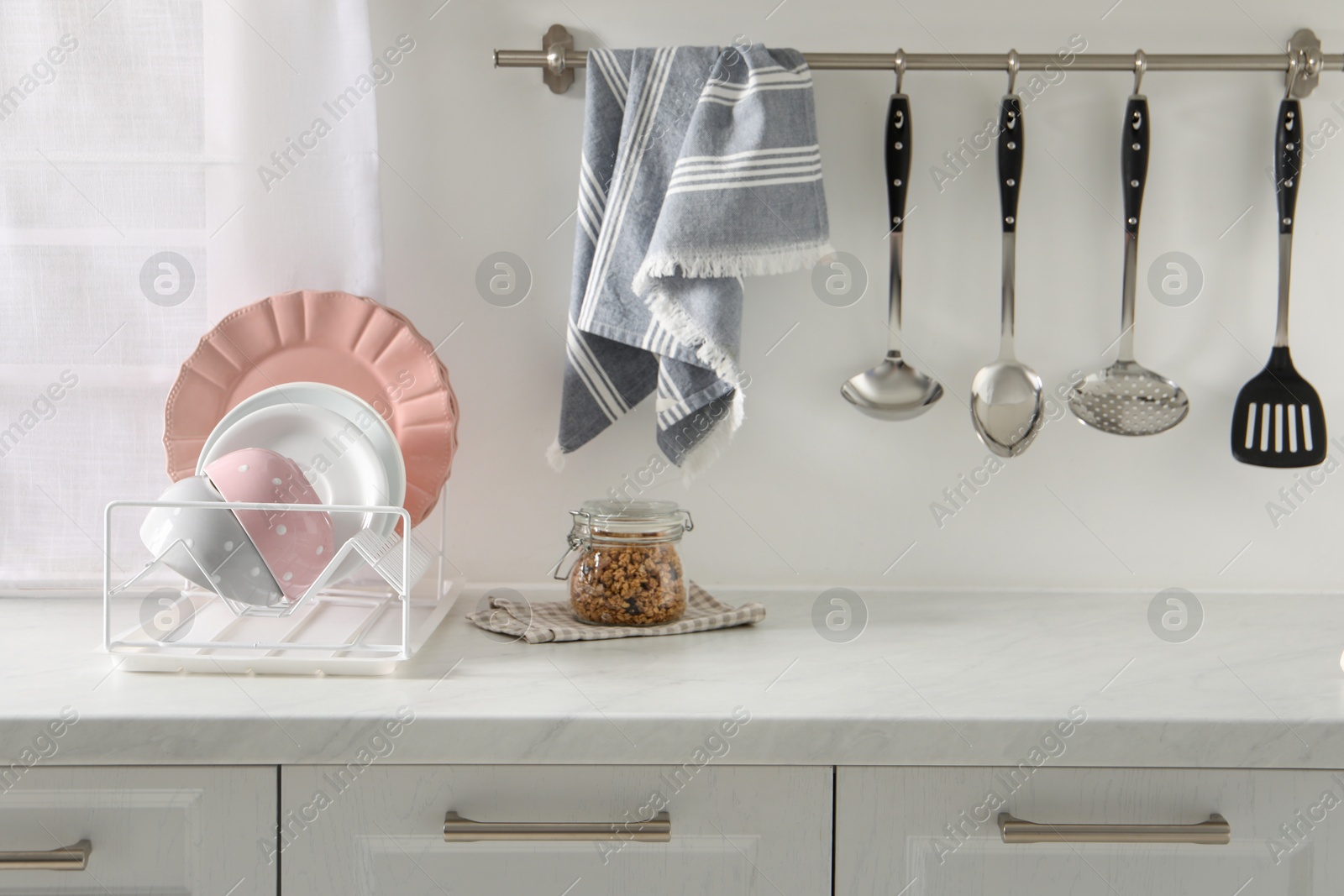 Photo of Drainer with different clean dishware on white table in kitchen