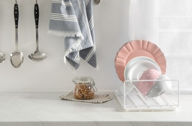 Photo of Drainer with different clean dishware on white table in kitchen