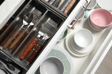 Photo of Clean plates, bowls and cutlery in drawers, top view