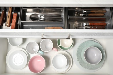Photo of Clean plates, bowls and cutlery in drawers, top view