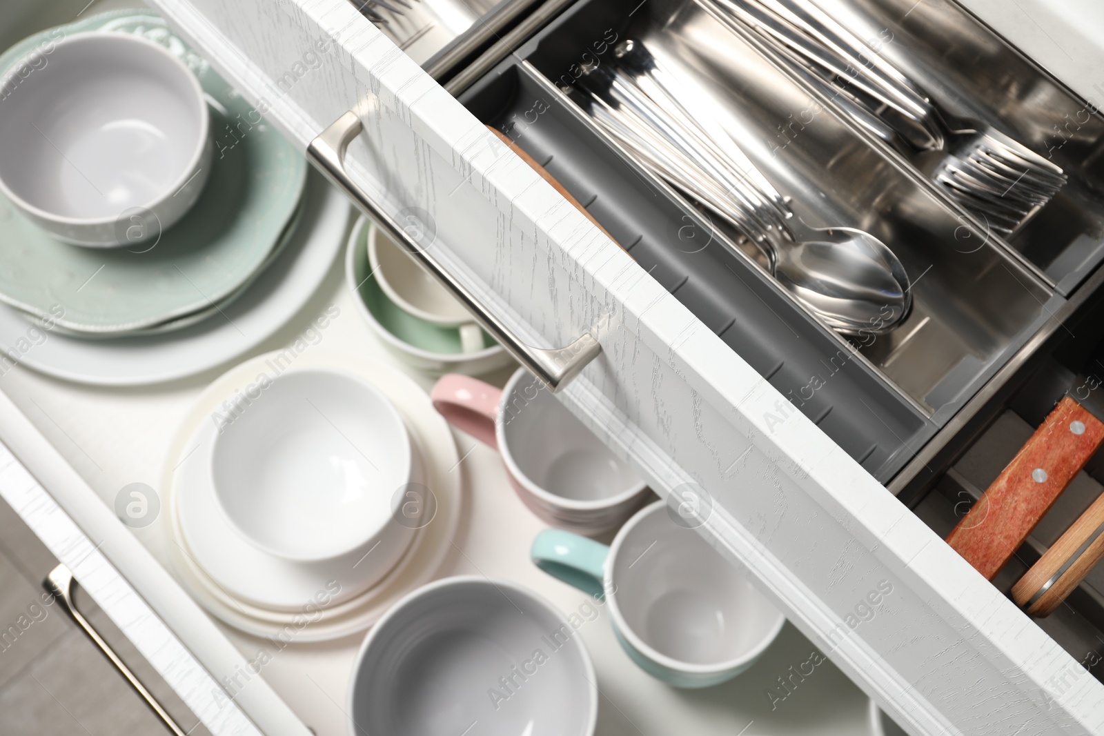 Photo of Ceramic dishware and cutlery in drawers indoors, above view