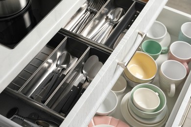 Photo of Ceramic dishware and cutlery in drawers indoors