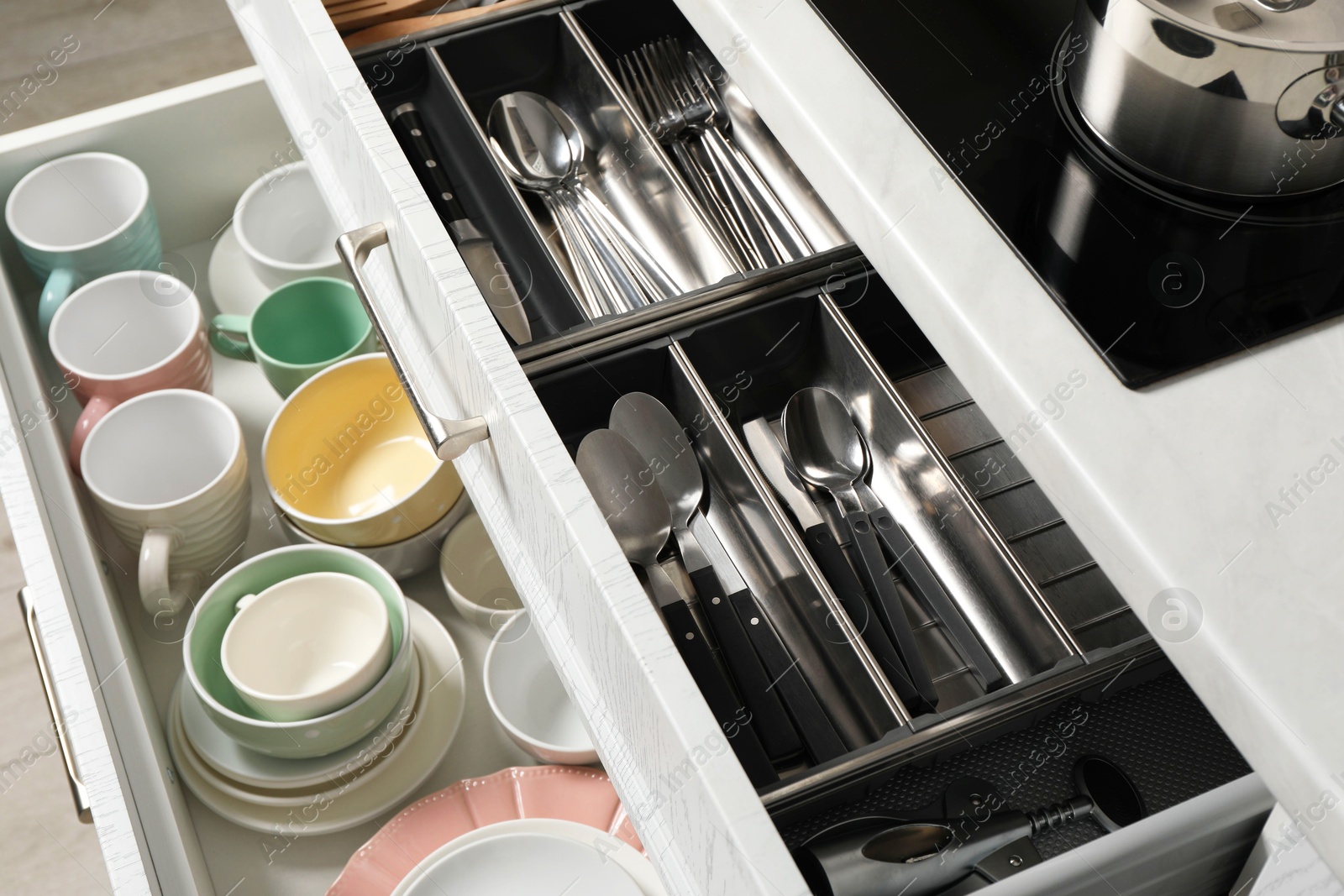 Photo of Ceramic dishware and cutlery in drawers indoors