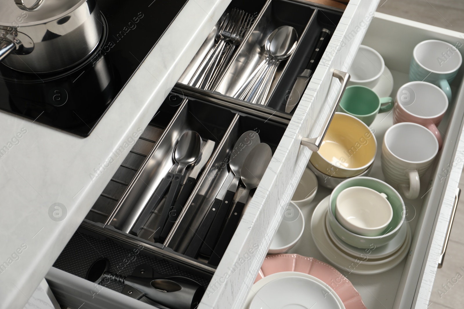 Photo of Ceramic dishware and cutlery in drawers indoors