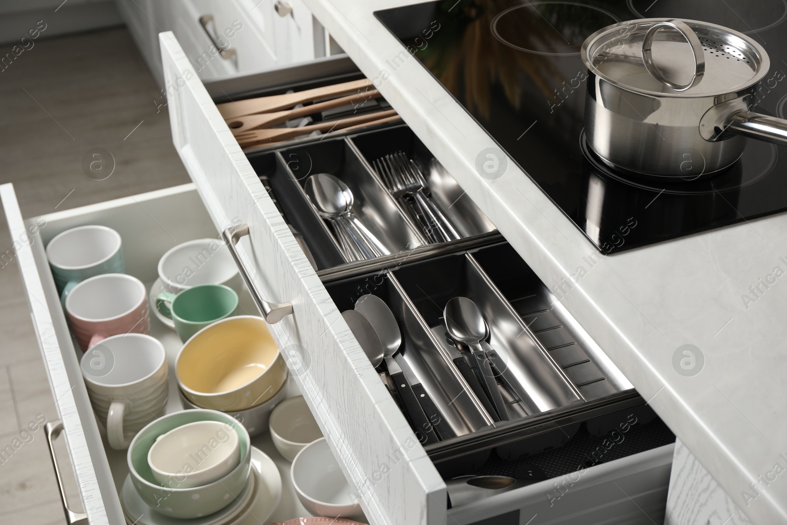 Photo of Ceramic dishware and cutlery in drawers in kitchen