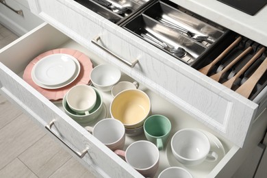 Photo of Ceramic dishware, utensils and cutlery in drawers indoors