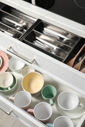 Photo of Ceramic dishware and cutlery in drawers indoors