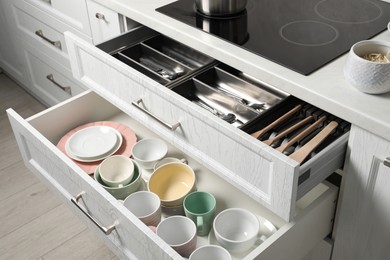 Photo of Ceramic dishware, utensils and cutlery in drawers in kitchen
