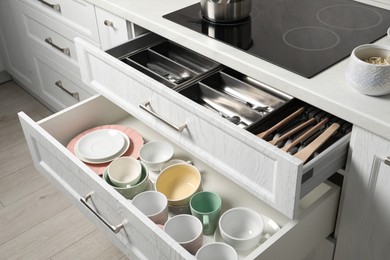 Ceramic dishware, utensils and cutlery in drawers in kitchen