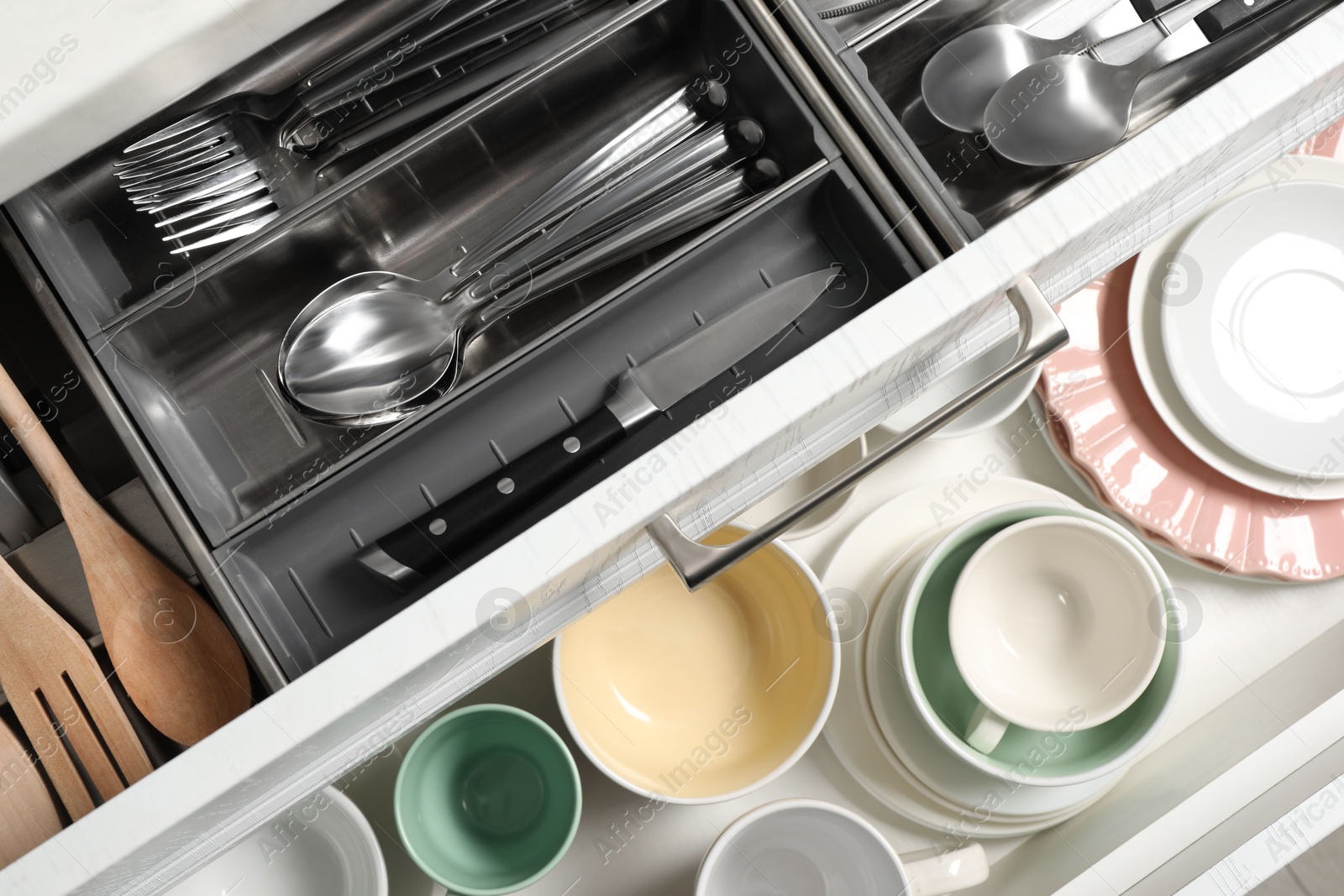 Photo of Ceramic dishware, utensils and cutlery in drawers, top view