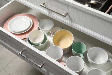 Photo of Ceramic dishware and cutlery in drawers indoors