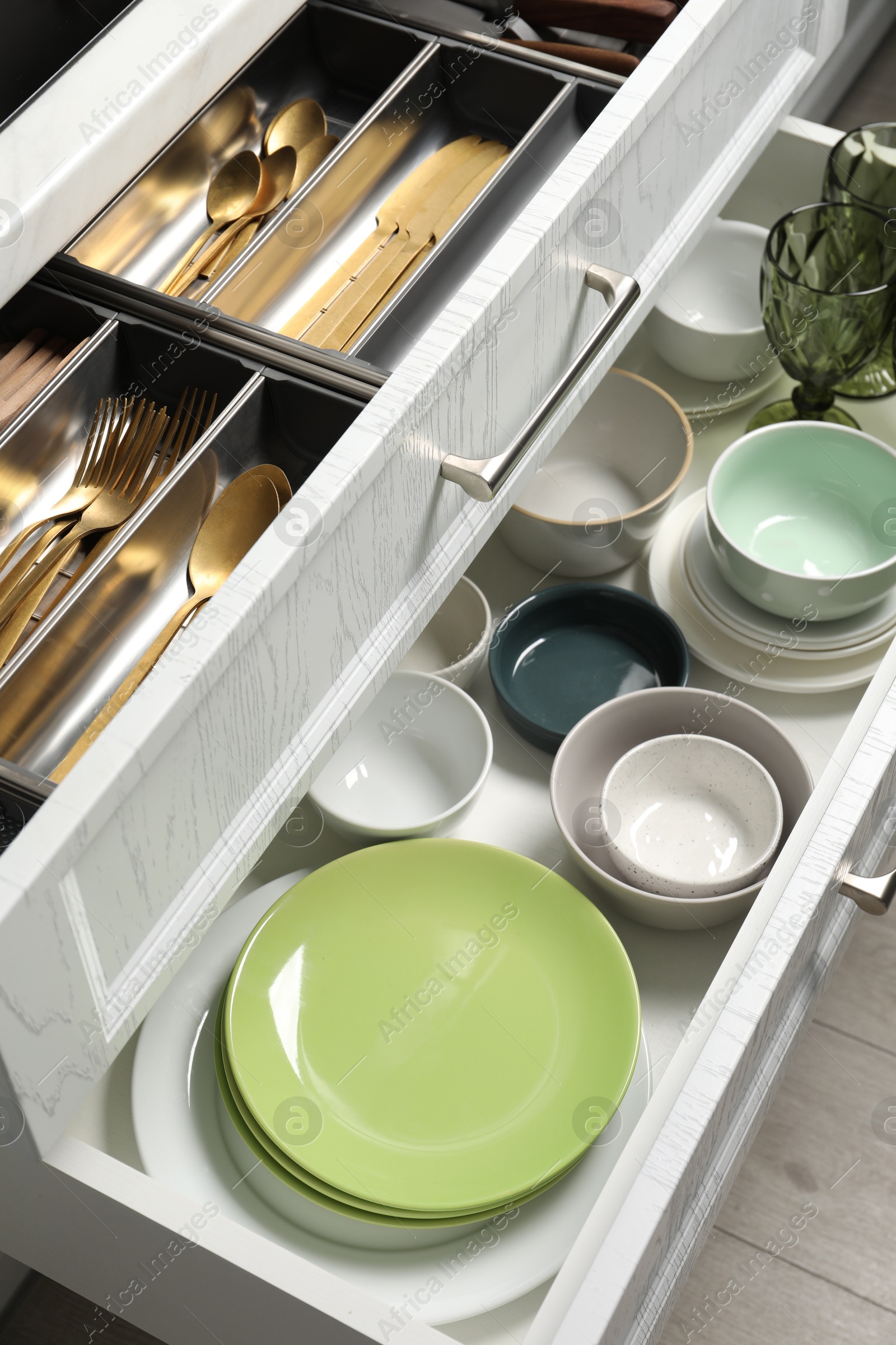 Photo of Ceramic dishware and cutlery in drawers indoors