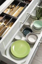 Photo of Ceramic dishware and cutlery in drawers indoors