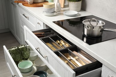 Photo of Ceramic dishware and cutlery in drawers in kitchen