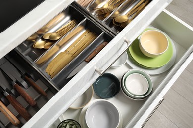 Photo of Ceramic dishware and cutlery in drawers indoors, above view