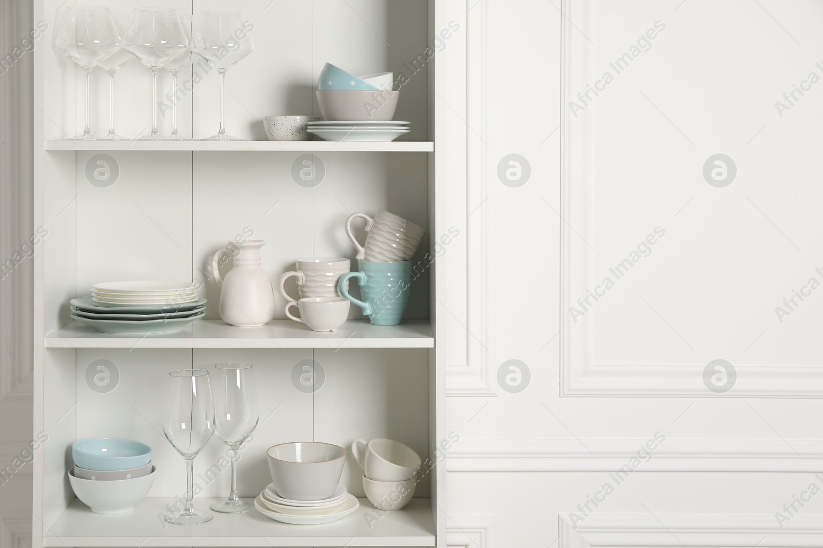 Photo of Different clean dishware and glasses on shelves in cabinet indoors