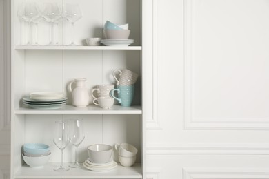 Different clean dishware and glasses on shelves in cabinet indoors