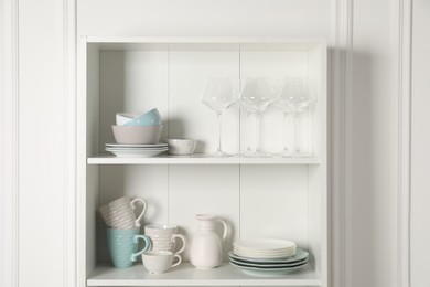 Photo of Different clean dishware and glasses on shelves in cabinet indoors