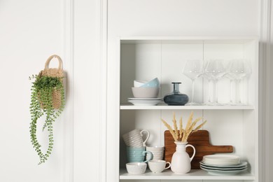 Photo of Different clean dishware and glasses on shelves in cabinet indoors