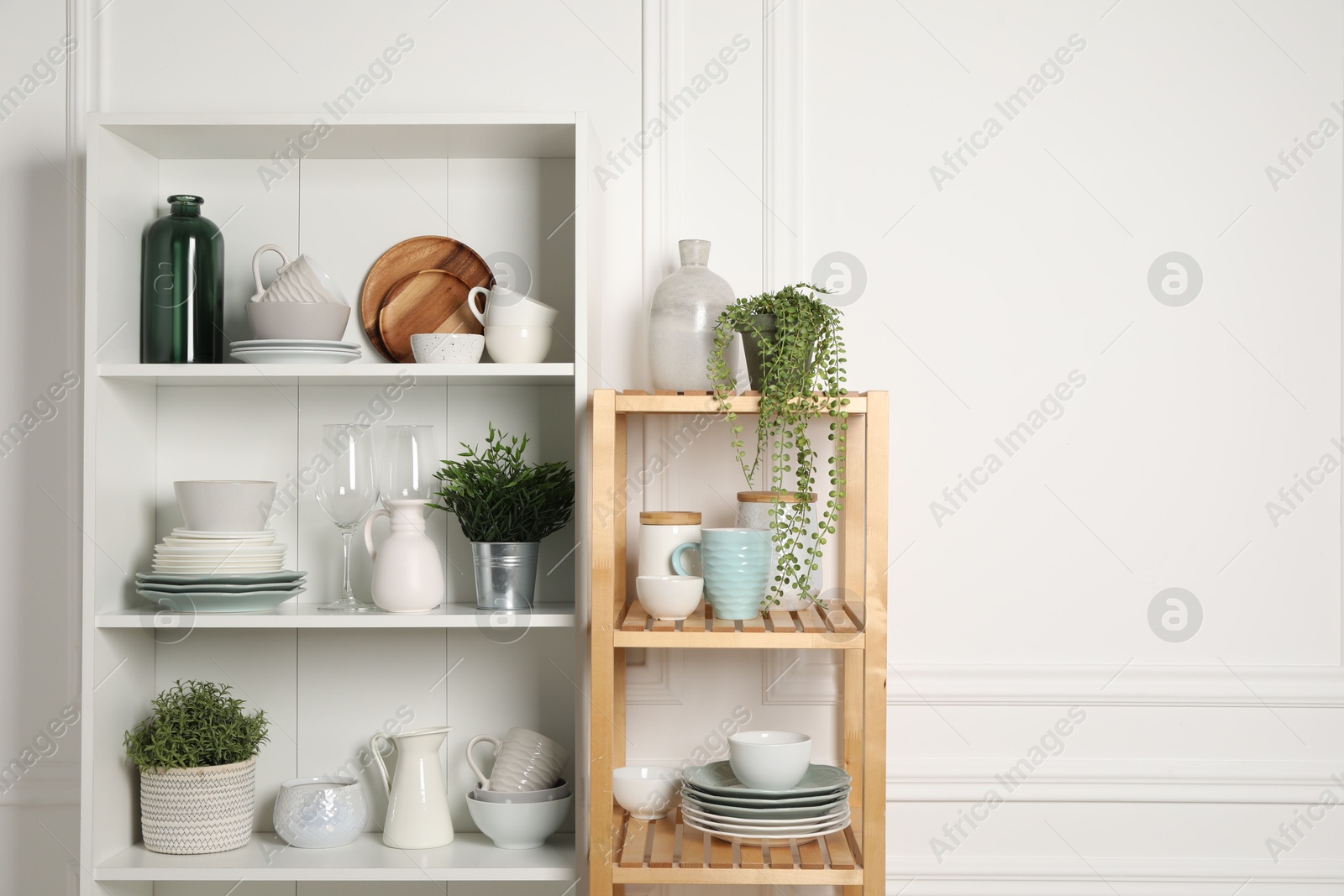 Photo of Different clean dishware and houseplants on shelves in cabinet indoors. Space for text