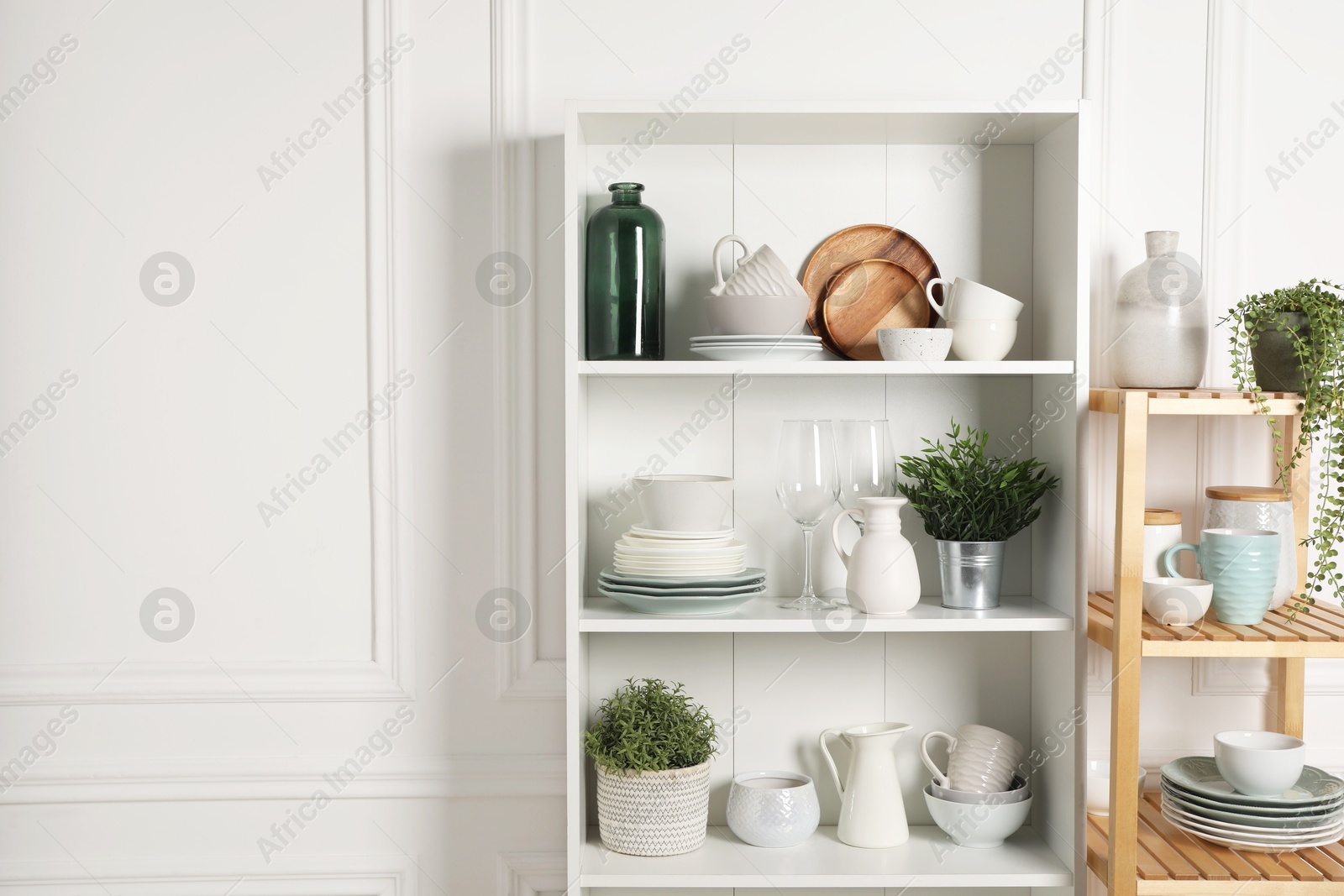 Photo of Different clean dishware and houseplants on shelves in cabinet indoors. Space for text