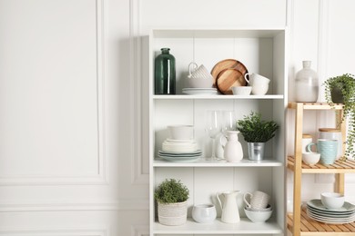 Different clean dishware and houseplants on shelves in cabinet indoors. Space for text