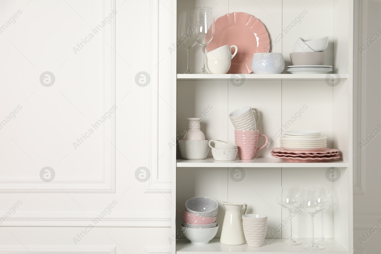 Photo of Different ceramic dishware and glasses on shelves in cabinet indoors. Space for text