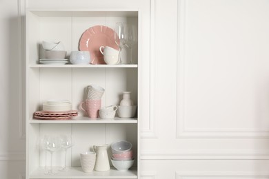 Different ceramic dishware and glasses on shelves in cabinet indoors. Space for text