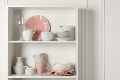 Different ceramic dishware and glasses on shelves in cabinet indoors