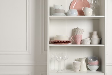 Different ceramic dishware and glasses on shelves in cabinet indoors. Space for text