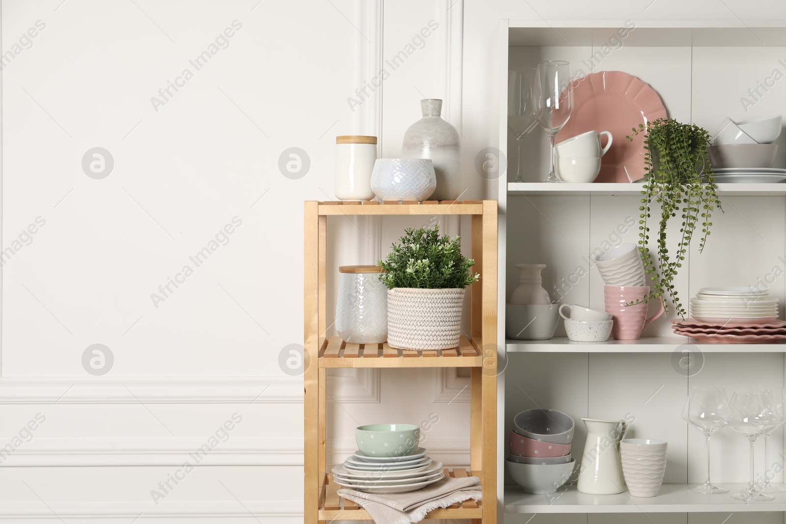 Photo of Different clean dishware and houseplants on shelves in cabinet indoors. Space for text