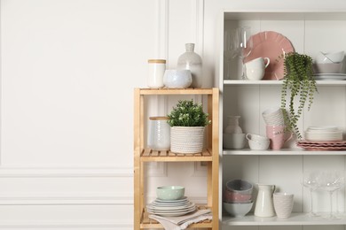 Different clean dishware and houseplants on shelves in cabinet indoors. Space for text