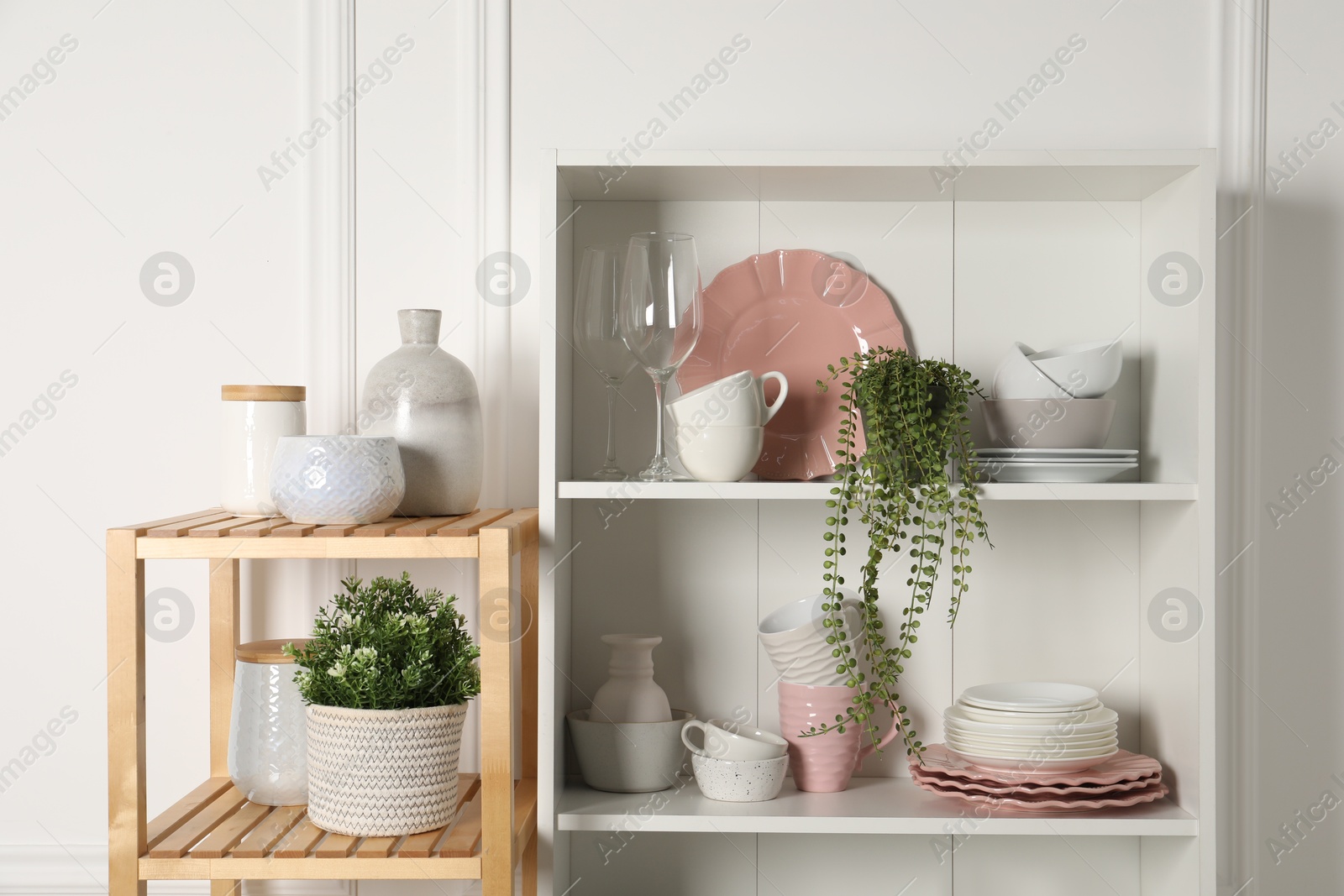 Photo of Different clean dishware and houseplants on shelves in cabinet indoors