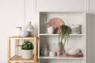 Different clean dishware and houseplants on shelves in cabinet indoors