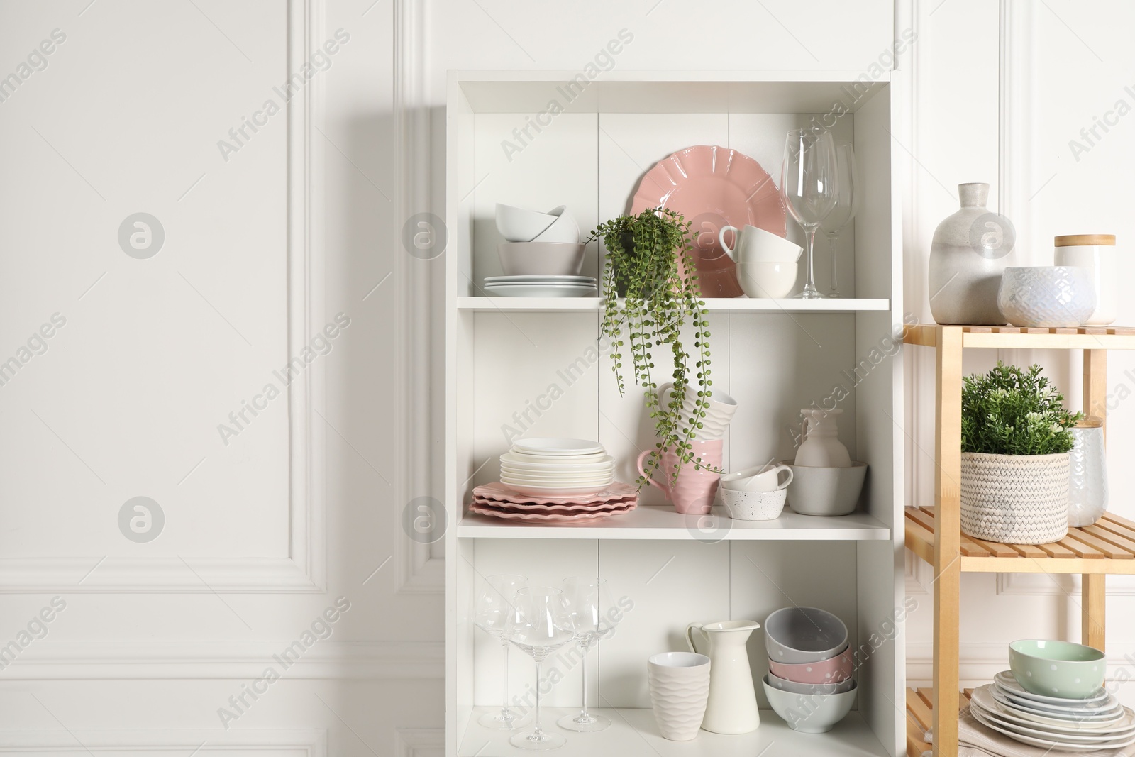 Photo of Different clean dishware and houseplants on shelves in cabinet indoors. Space for text