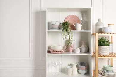 Different clean dishware and houseplants on shelves in cabinet indoors. Space for text