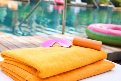 Photo of Beach towels, sunglasses and sunscreen on sun lounger near outdoor swimming pool. Luxury resort