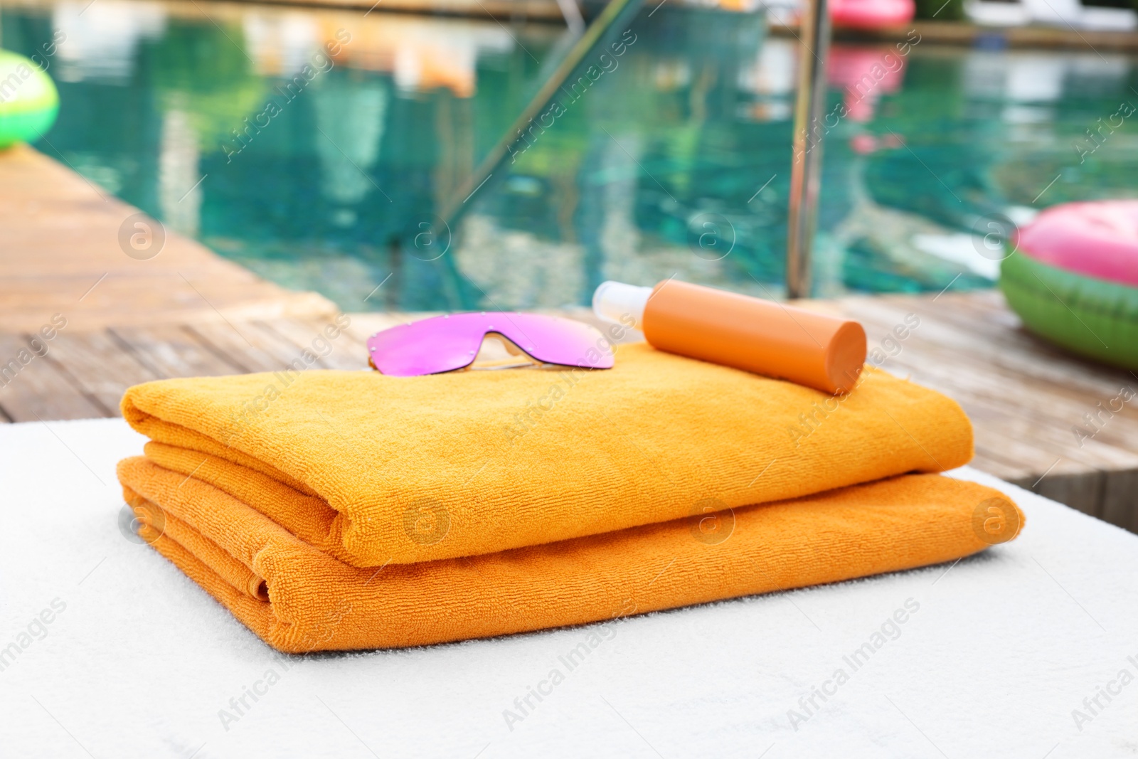 Photo of Beach towels, sunglasses and sunscreen on sun lounger near outdoor swimming pool, selective focus. Luxury resort