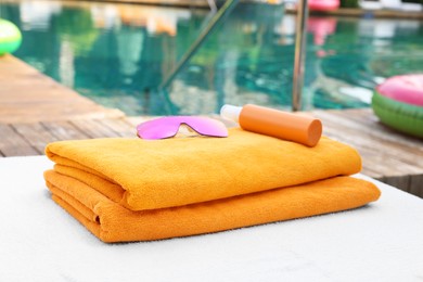 Beach towels, sunglasses and sunscreen on sun lounger near outdoor swimming pool, selective focus. Luxury resort