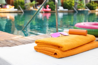 Beach towels, sunglasses and sunscreen on sun lounger near outdoor swimming pool at luxury resort. Space for text